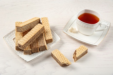 Photo of Plate of delicious wafers with cup of tea on white wooden background