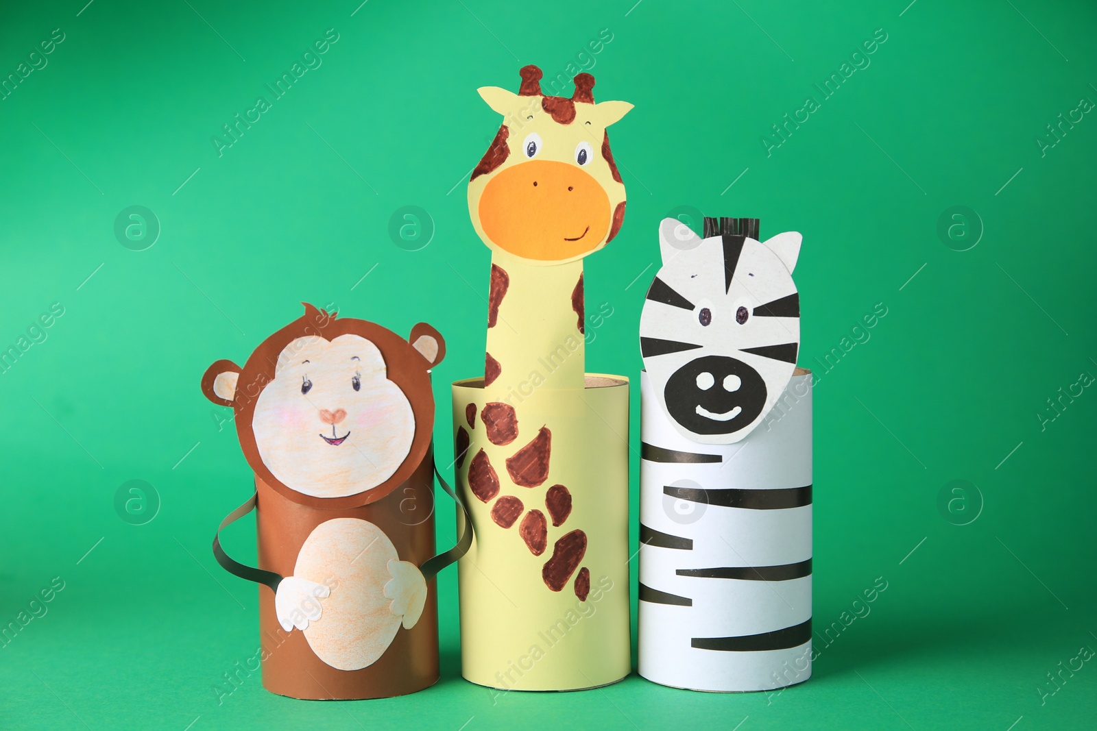 Photo of Toy monkey, giraffe and zebra made from toilet paper hubs on green background. Children's handmade ideas