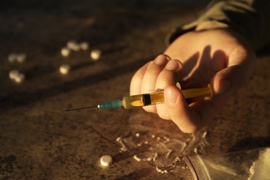 Addicted man with syringe near drugs at grey textured table, closeup. Space for text