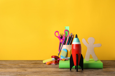 Photo of Bright toy rocket and school supplies on wooden desk. Space for text