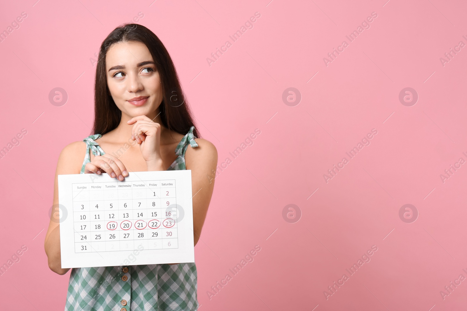 Photo of Young woman holding calendar with marked menstrual cycle days on pink background. Space for text