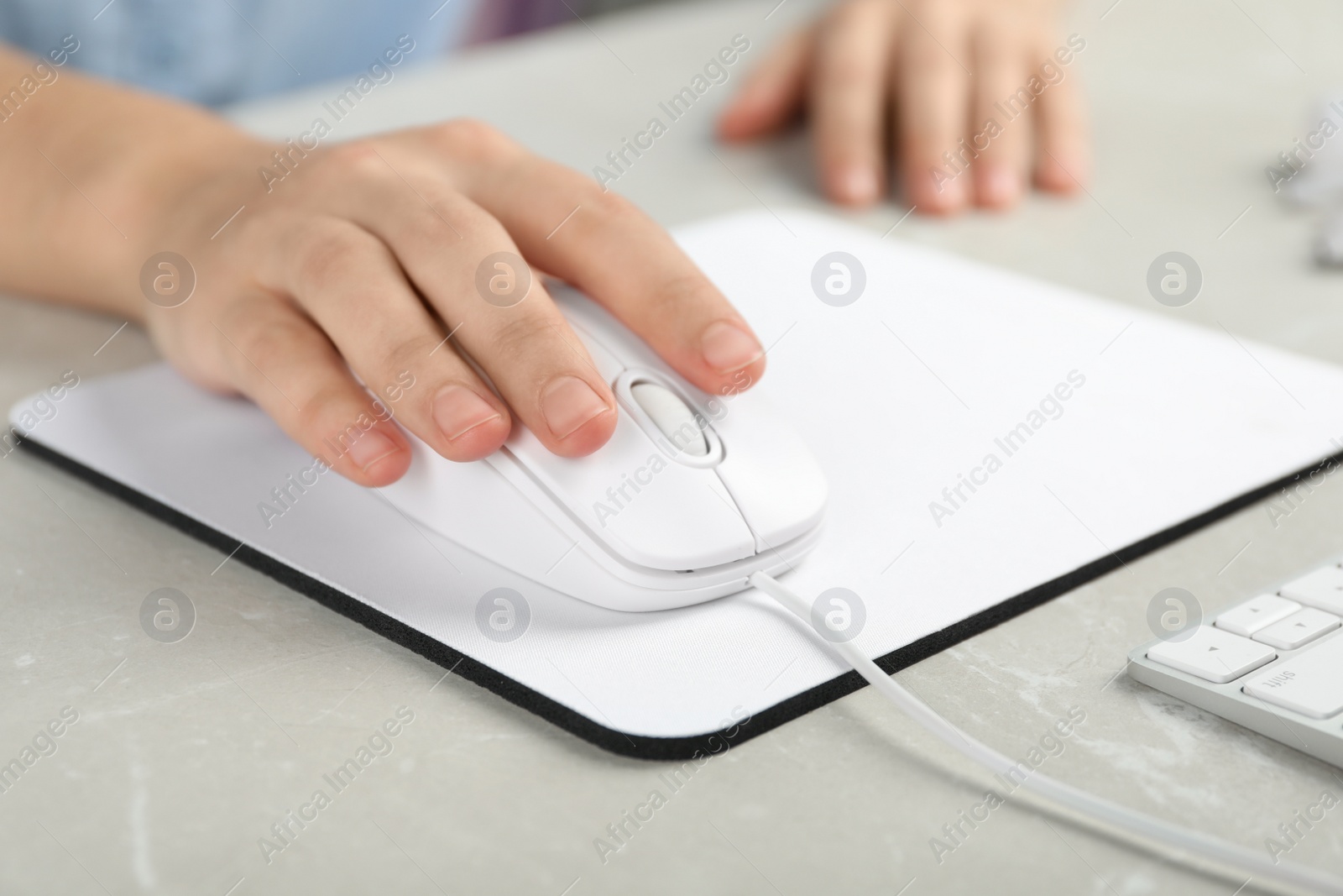 Photo of Woman using wired computer mouse on pad at light grey marble table, closeup