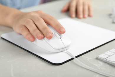 Photo of Woman using wired computer mouse on pad at light grey marble table, closeup