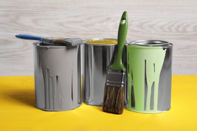 Photo of Cans of paints and brushes on yellow wooden table