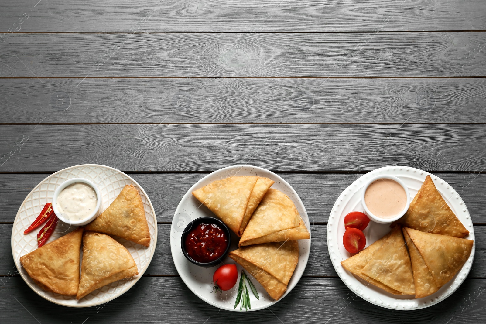 Photo of Fresh delicious crispy samosas served on grey wooden table, flat lay. Space for text