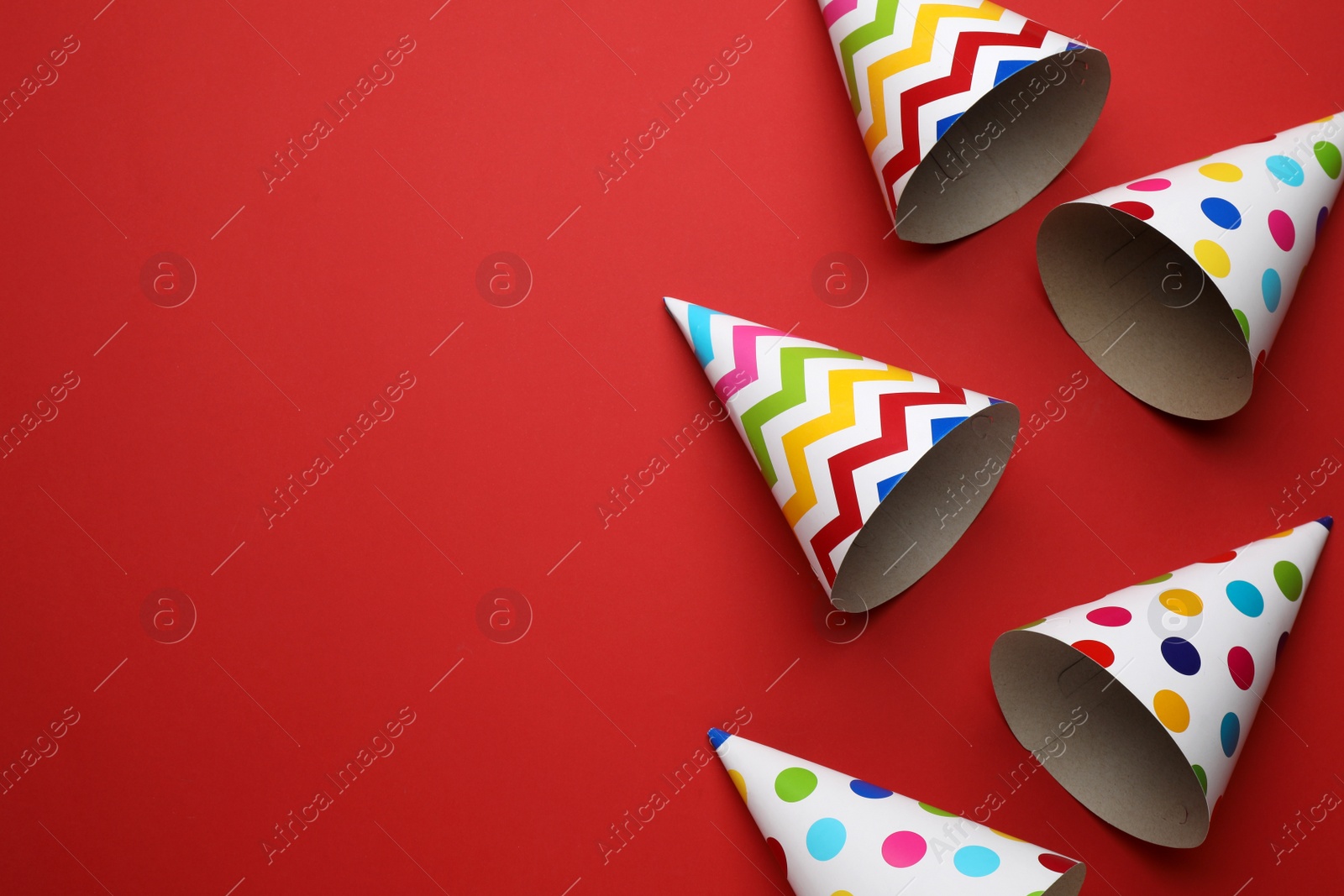 Photo of Bright party hats on red background, flat lay. Space for text