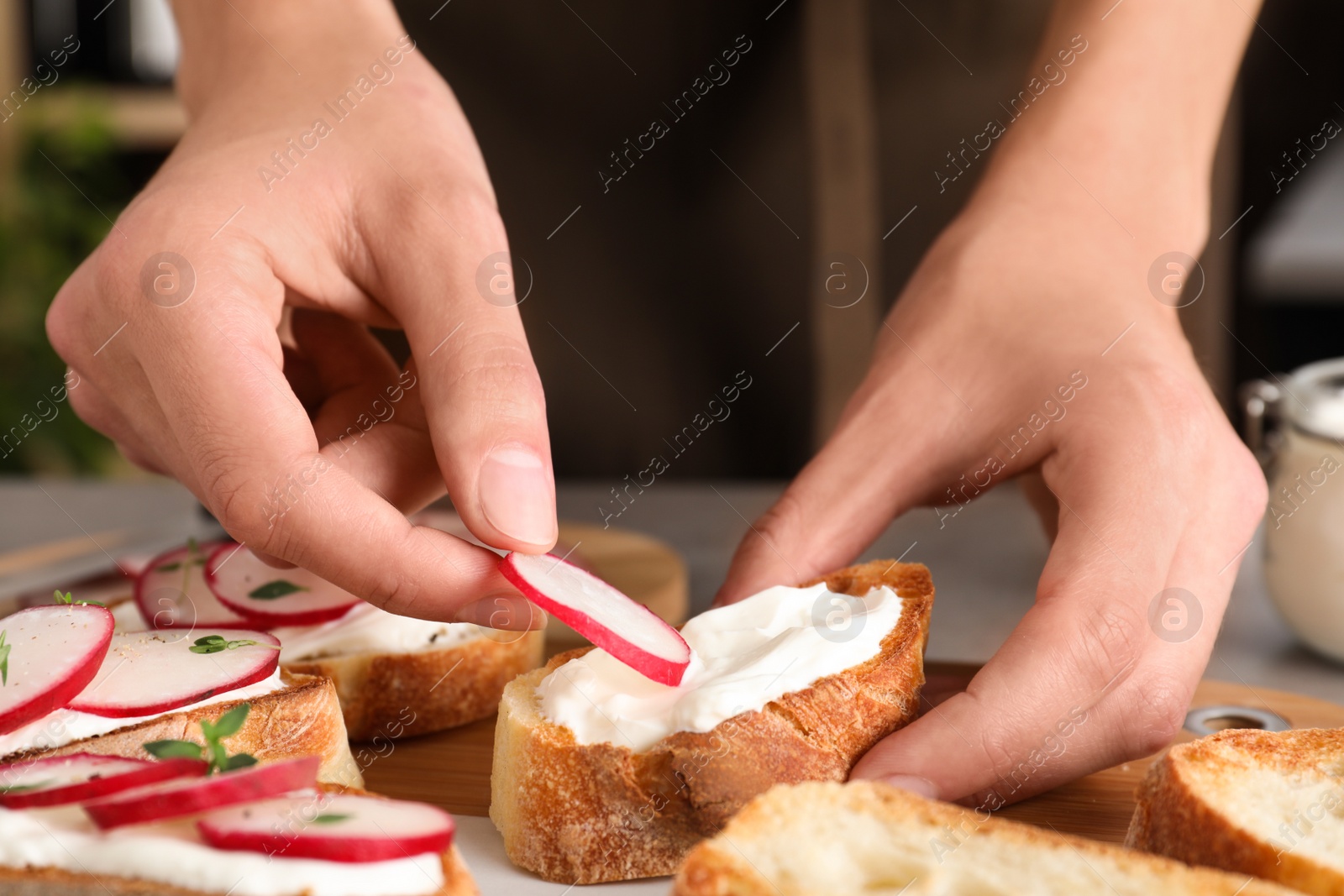 Photo of Woman preparing bruschetta with radishes at table, closeup