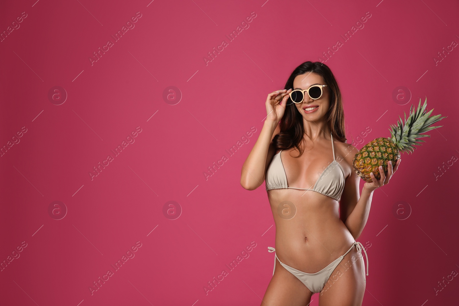 Photo of Beautiful woman in stylish bikini with pineapple on crimson background. Space for text