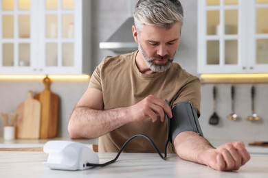 Photo of Man measuring blood pressure at table indoors