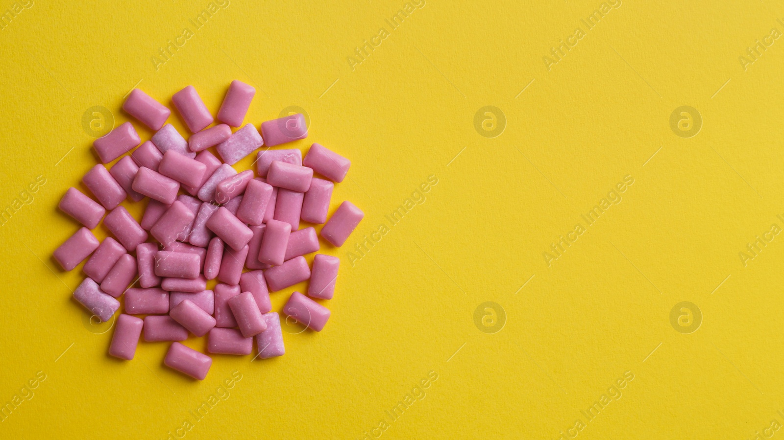 Photo of Sweet chewing gums on yellow background, flat lay. Space for text