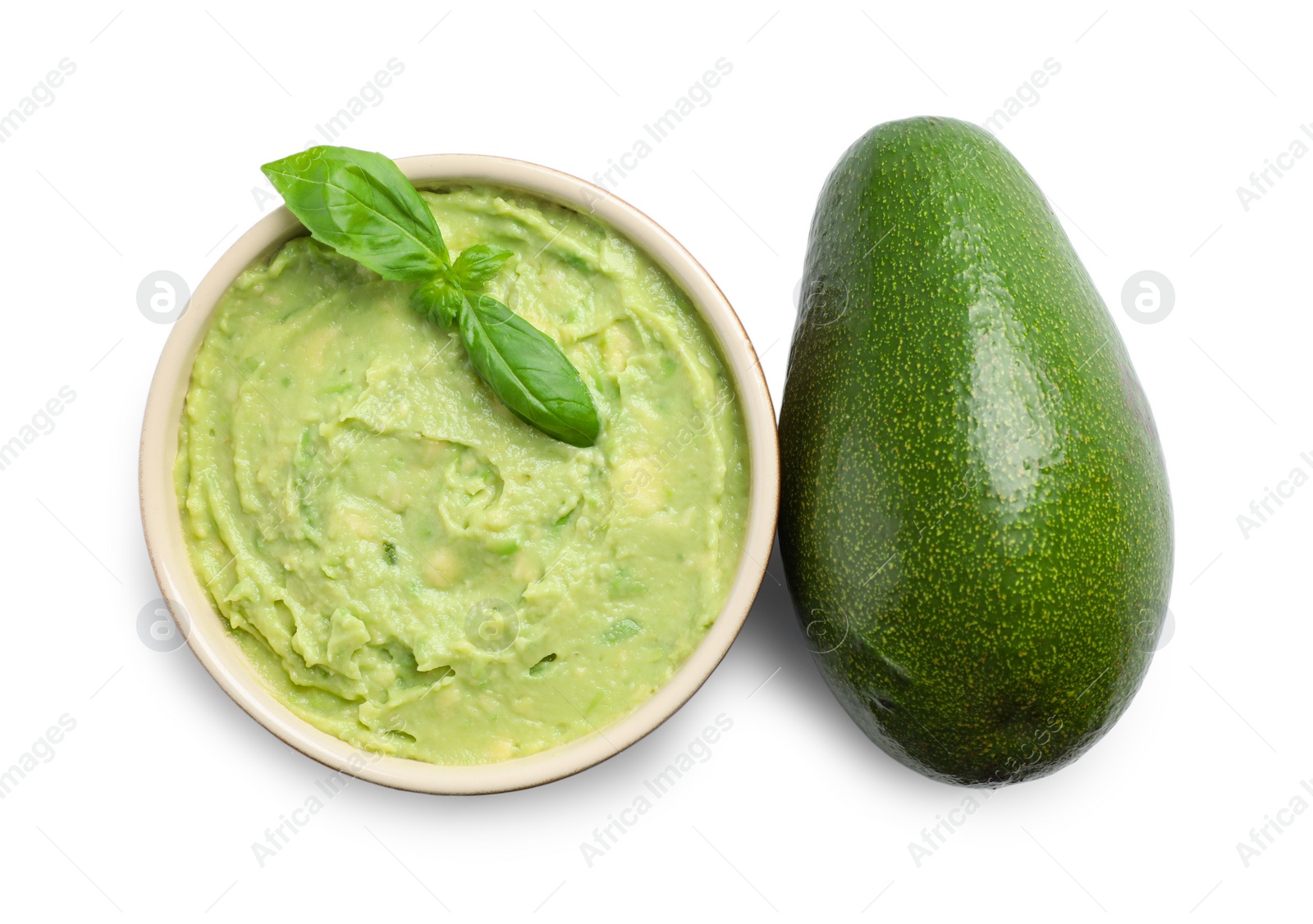 Photo of Bowl of tasty guacamole with basil and whole avocado on white background, top view