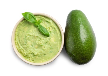 Photo of Bowl of tasty guacamole with basil and whole avocado on white background, top view