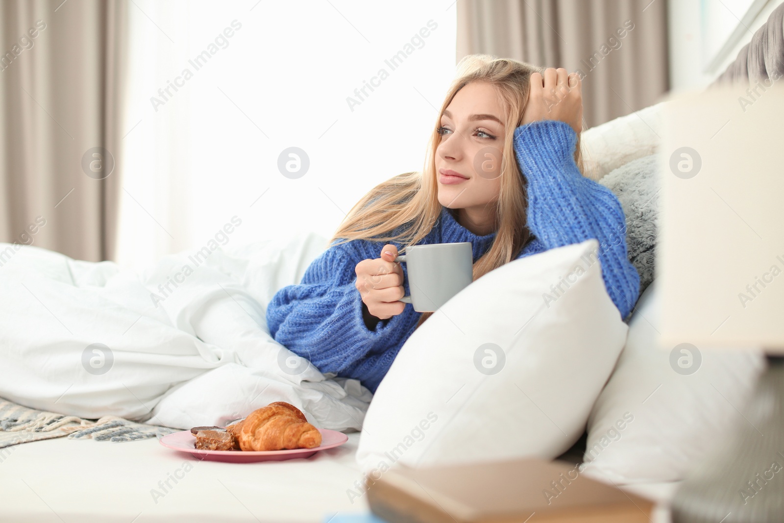 Photo of Beautiful young woman lying with breakfast in bed at home. Winter atmosphere