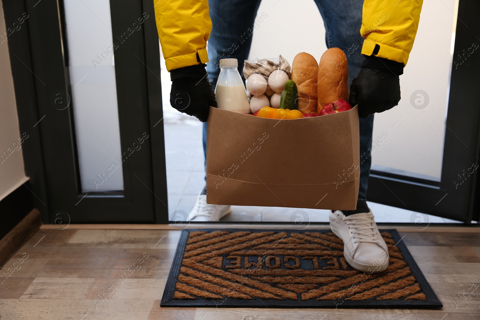 Photo of Courier bring paper bag with food to doorway, closeup. Delivery service during quarantine due Covid-19 outbreak