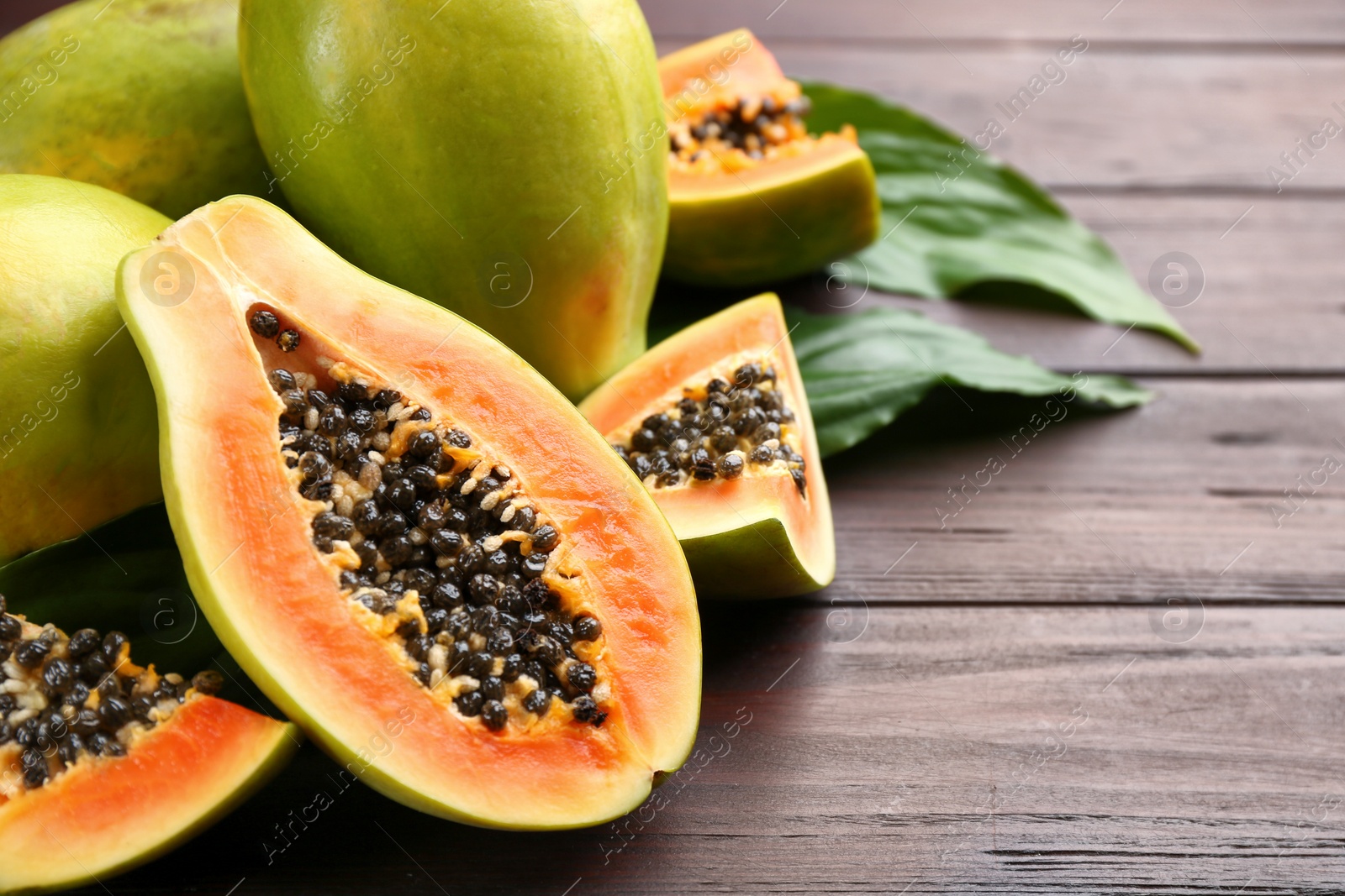 Photo of Fresh ripe papaya fruits with green leaves on wooden table. Space for text