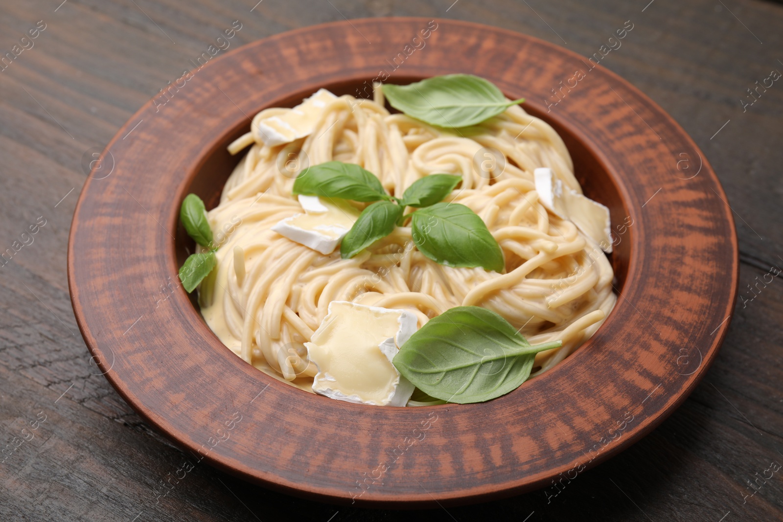 Photo of Delicious pasta with brie cheese and basil leaves on wooden table, closeup