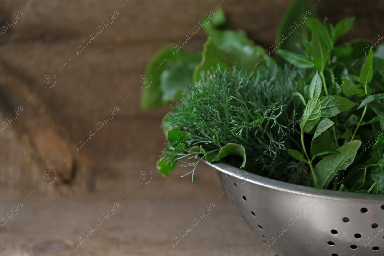Photo of Different herbs in colander on wooden table, closeup. Space for text