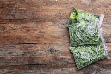 Different frozen vegetables on wooden table, flat lay. Space for text