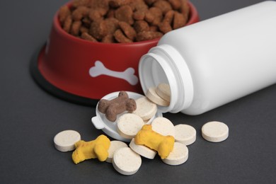 Photo of Bottle with vitamins and dry pet food in bowl on grey background, closeup