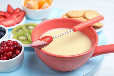 Photo of Fork with strawberry dipped into white chocolate fondue and ceramic pot on table