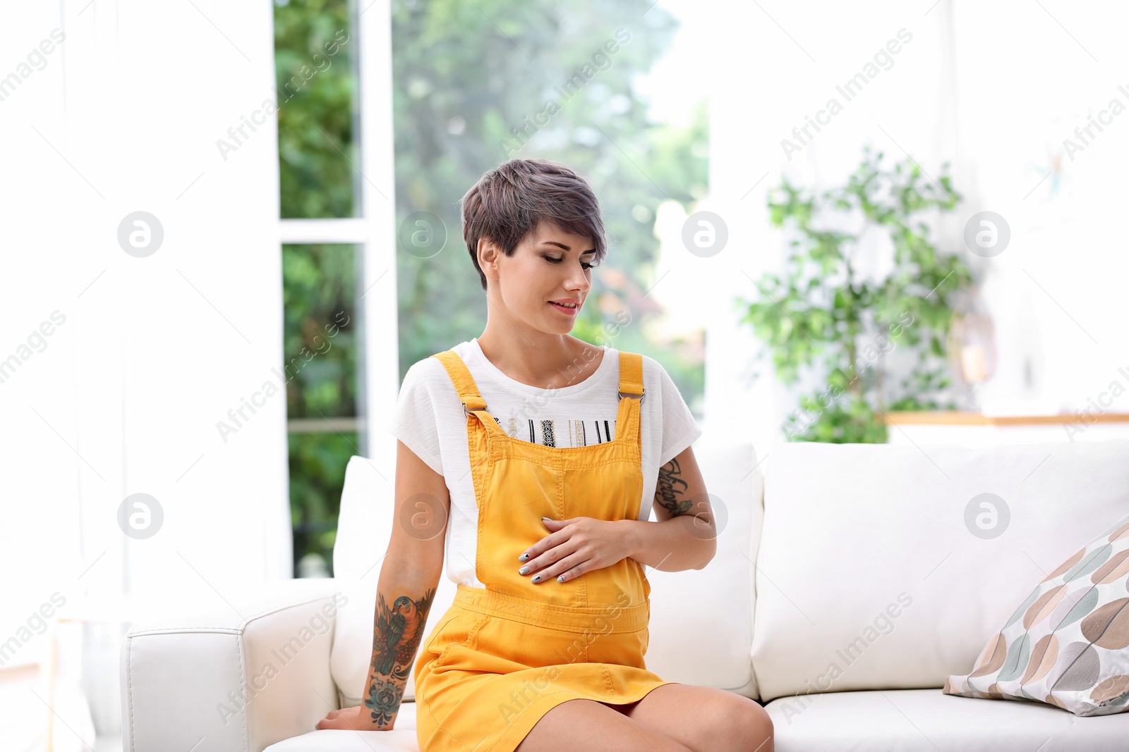 Photo of Trendy pregnant woman with tattoos on sofa indoors