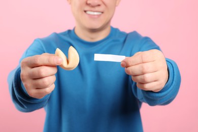 Photo of Happy man holding tasty fortune cookie with prediction on pink background, closeup