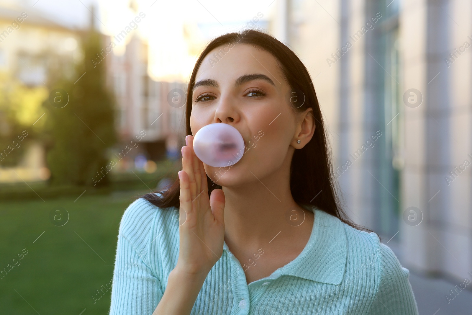 Photo of Beautiful woman blowing gum near building outdoors