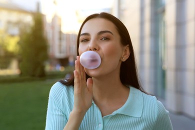 Beautiful woman blowing gum near building outdoors