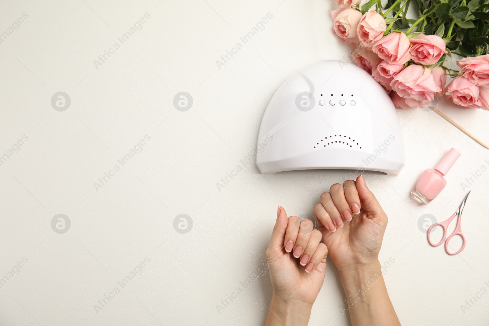 Photo of Woman doing manicure with ultraviolet nail lamp at white table, top view. Space for text