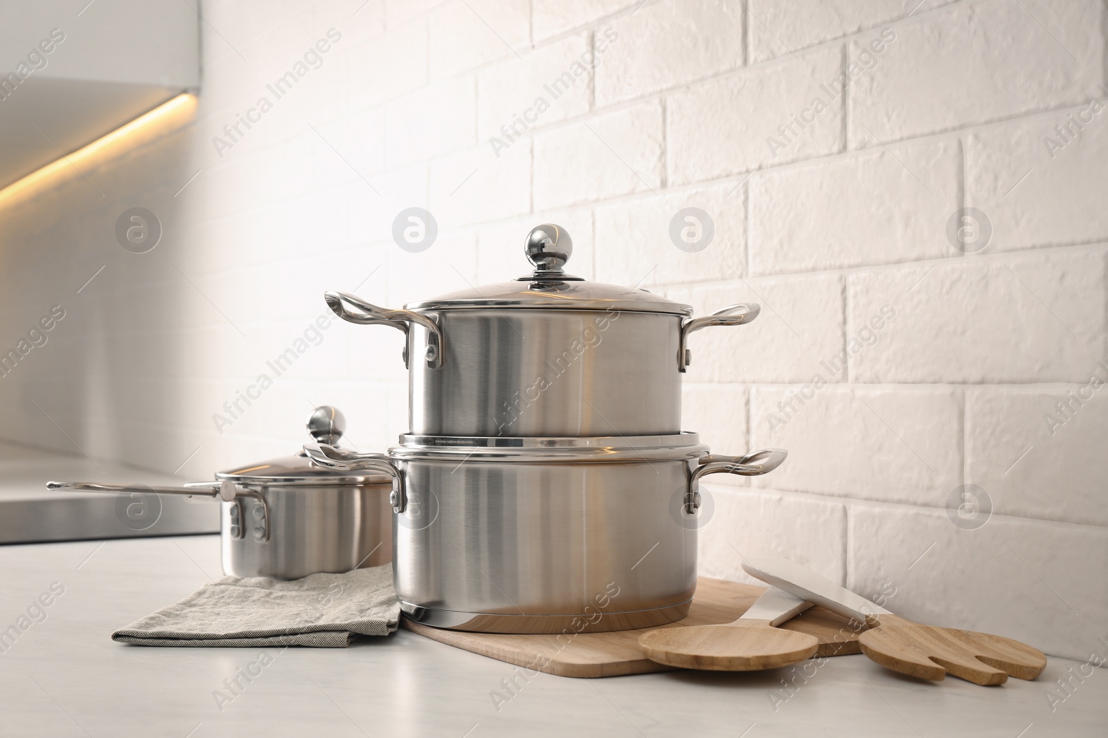 Photo of Set of stainless steel cookware and kitchen utensils on table near white brick wall