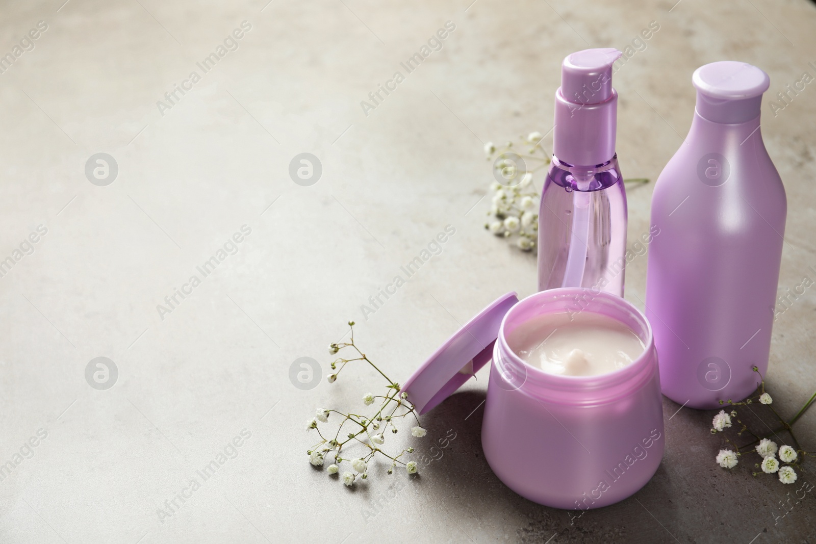 Photo of Set of hair cosmetic products and flowers on grey stone table. Space for text