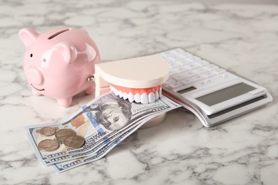 Photo of Educational dental typodont model with money, piggy bank and calculator on white marble table. Expensive treatment