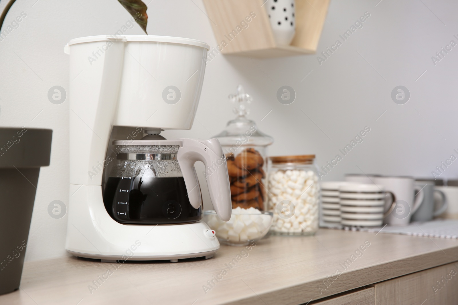 Photo of Modern coffeemaker and cups on wooden table indoors