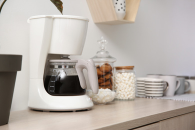 Modern coffeemaker and cups on wooden table indoors