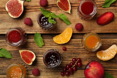 Photo of Jars of different jams and fresh ingredients on wooden table, flat lay