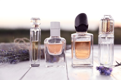 Bottles of luxury perfume and lavender flowers on white wooden table outdoors