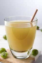 Photo of Tasty gooseberry juice on white wooden table against light background, closeup