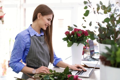 Photo of Young florist working with laptop in flower shop