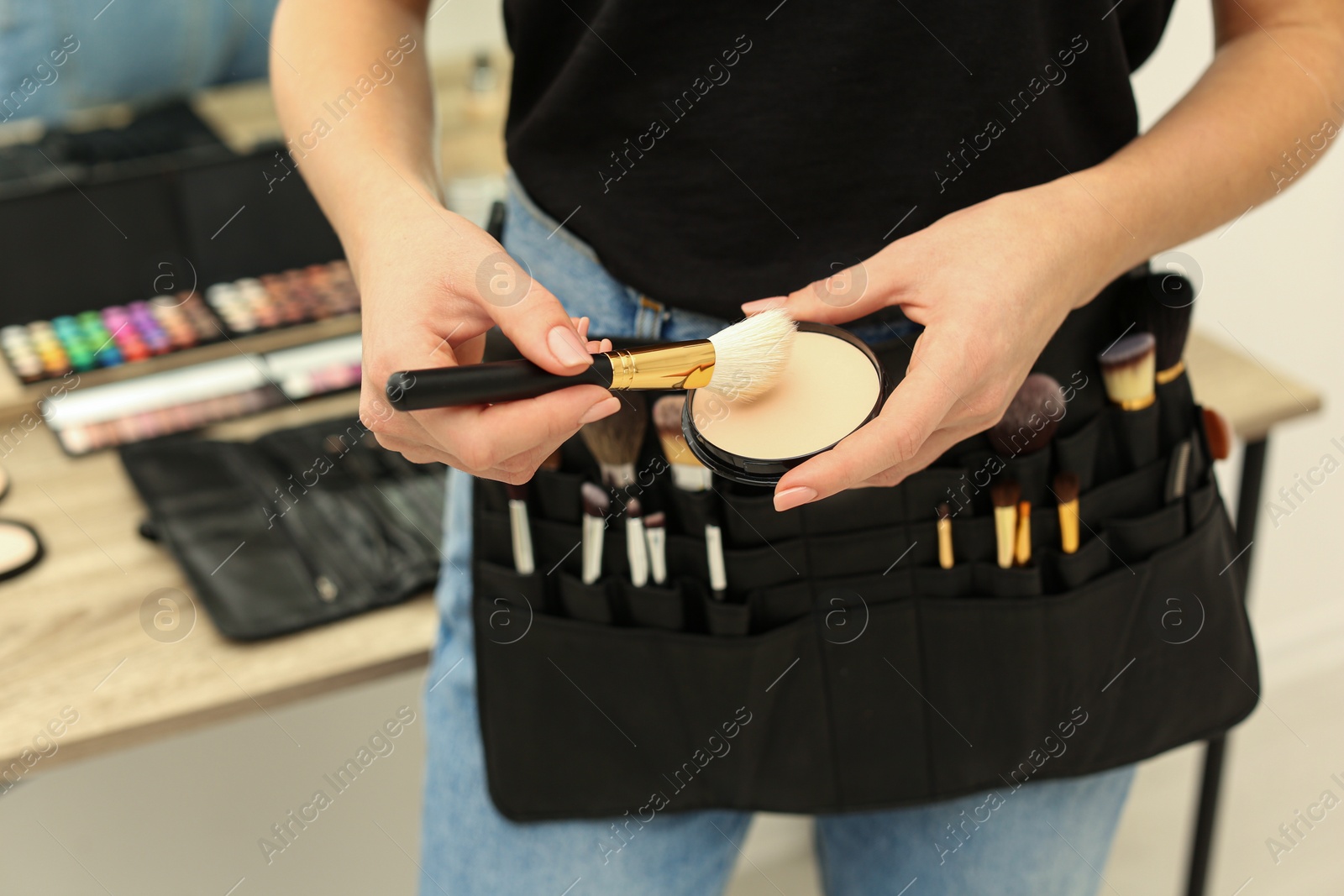 Photo of Professional makeup artist with face powder and belt organizer full of tools in studio, closeup