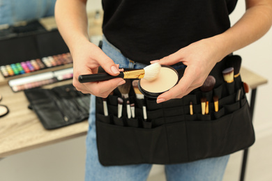 Photo of Professional makeup artist with face powder and belt organizer full of tools in studio, closeup