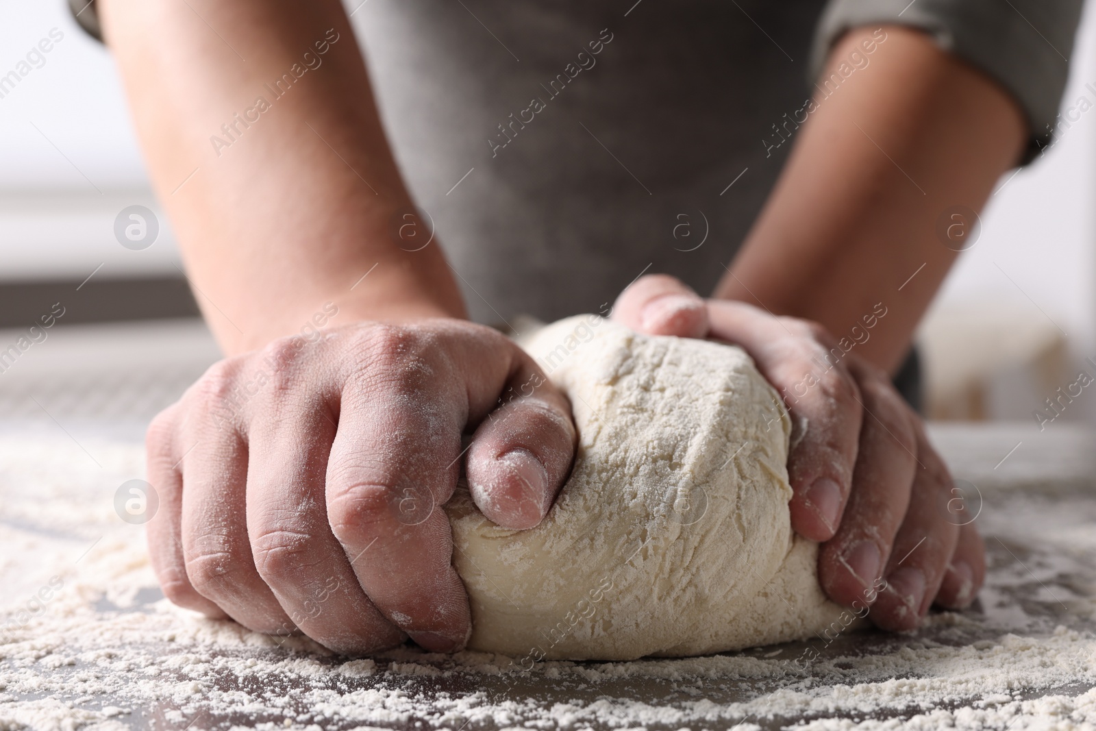 Photo of Man kneading dough at table in kitchen, closeup