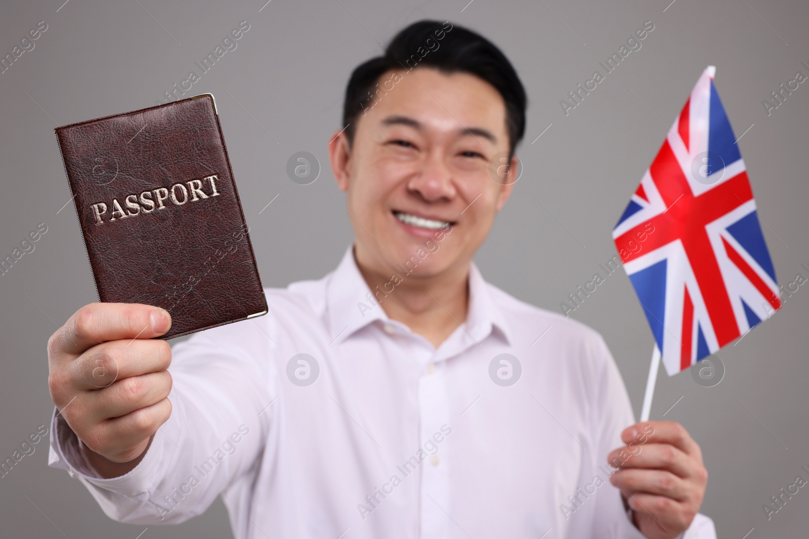 Photo of Immigration. Happy man with passport and flag of United Kingdom on grey background, selective focus