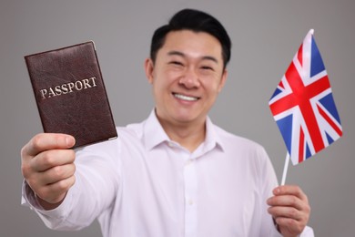 Photo of Immigration. Happy man with passport and flag of United Kingdom on grey background, selective focus