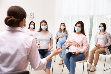 Photo of Group of pregnant women in protective masks with doctor at courses for expectant mothers indoors