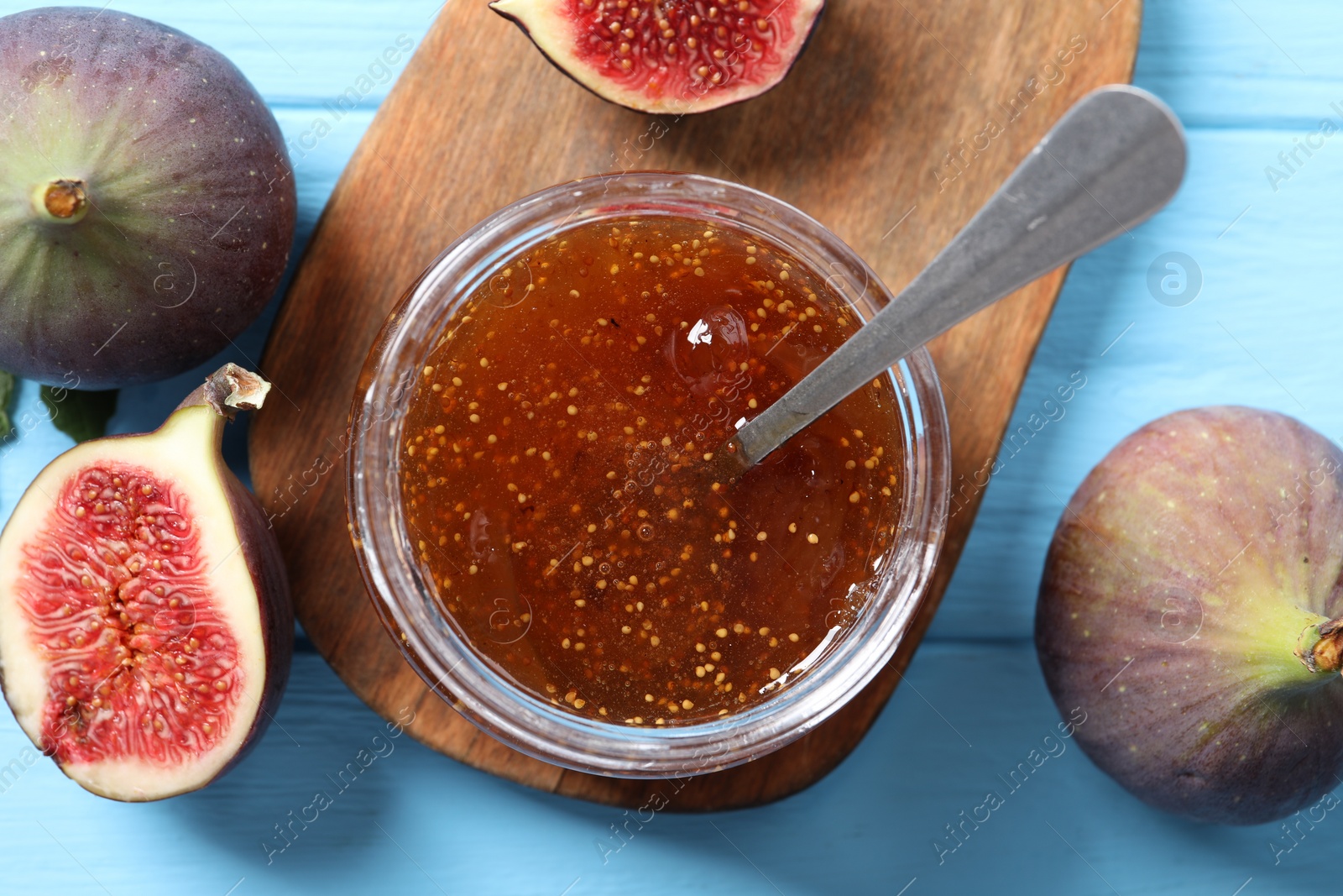 Photo of Jar of tasty sweet jam and fresh figs on light blue wooden table, flat lay