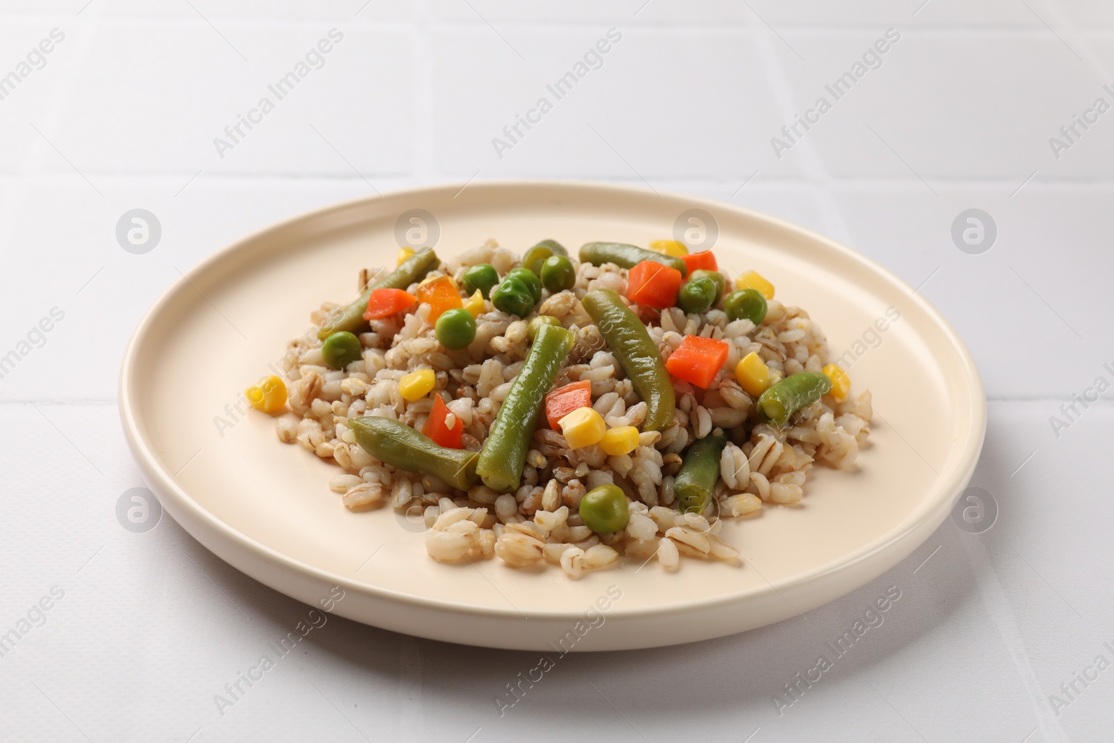 Photo of Delicious pearl barley with vegetables on white tiled table, closeup