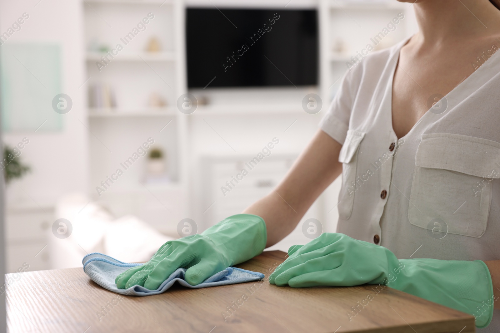 Photo of Woman with microfiber cloth cleaning wooden chest of drawers in room, closeup