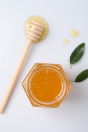 Photo of Tasty honey in glass jar, dipper and leaves isolated on white, top view