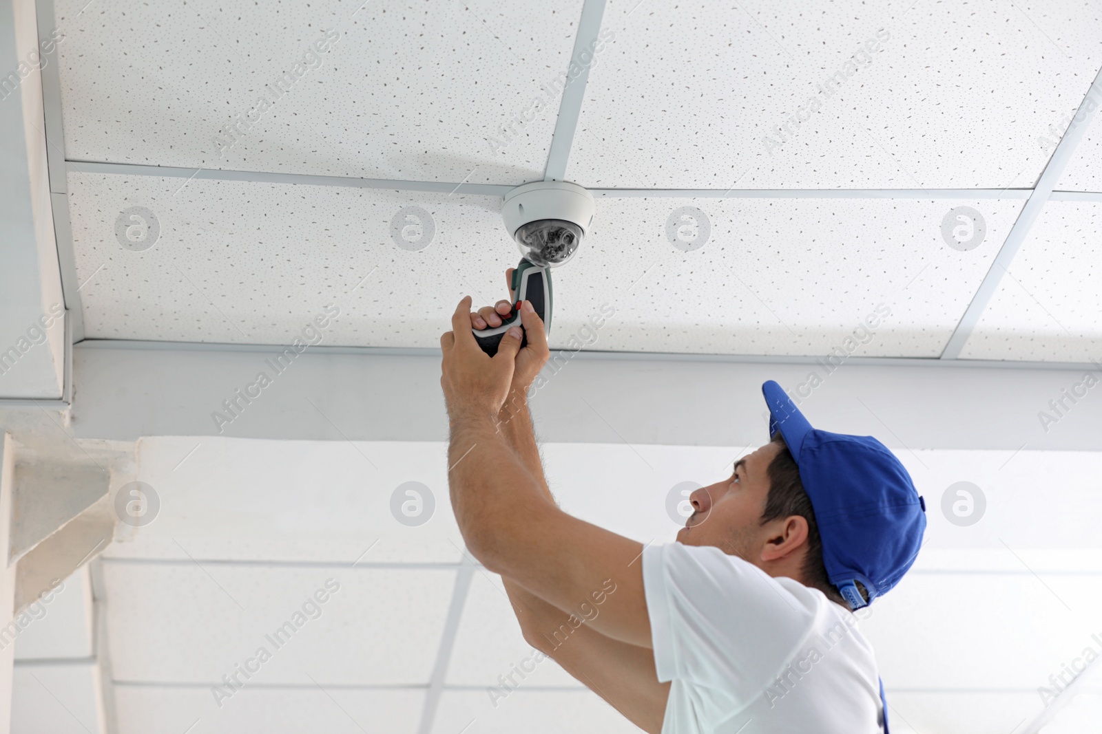 Photo of Technician installing CCTV camera on ceiling indoors