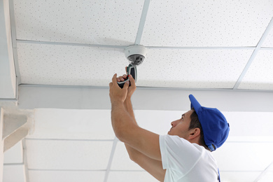 Technician installing CCTV camera on ceiling indoors